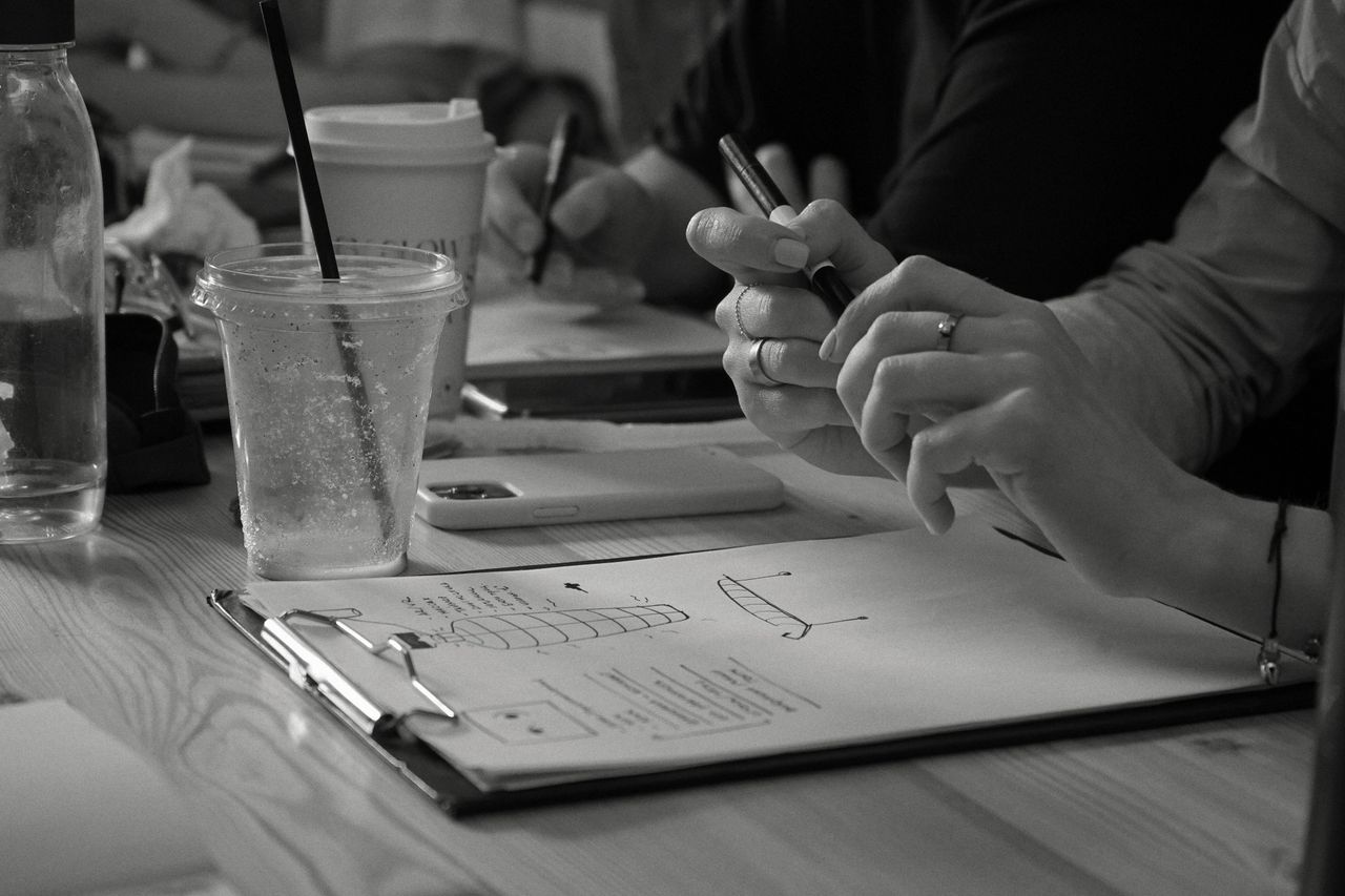 Services-02 Close-up of hands writing notes in an office setting with drinks on a table.